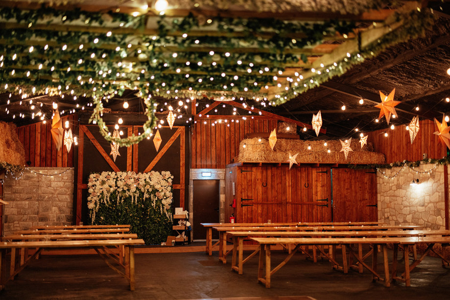 Barn ceremony room with benches and decorated with stars, fairy lights and leaves wrapped around beams
